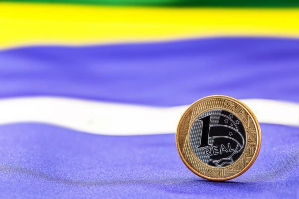 Imagem colorida de uma moeda de 1 real sobre uma bandeira do Brasil - Metrópoles