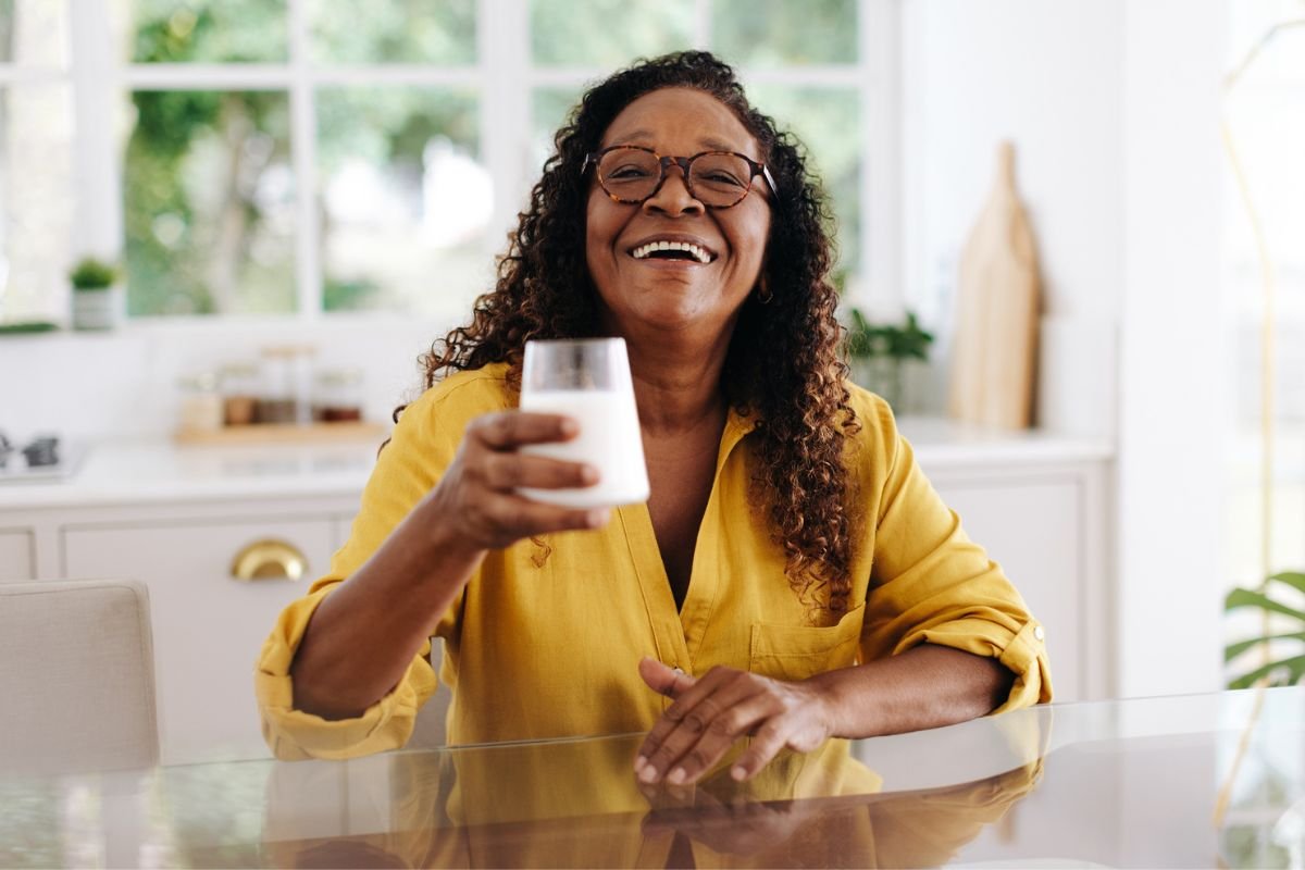 mulher com blusa amarela segurando um copo de leite