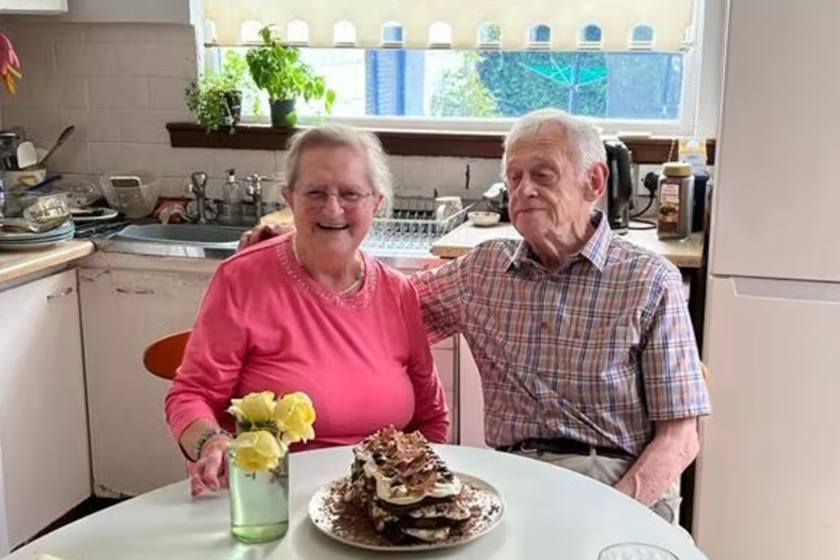 Casal de idosos sentados em mesa de cozinha sorrindo - Metrópoles