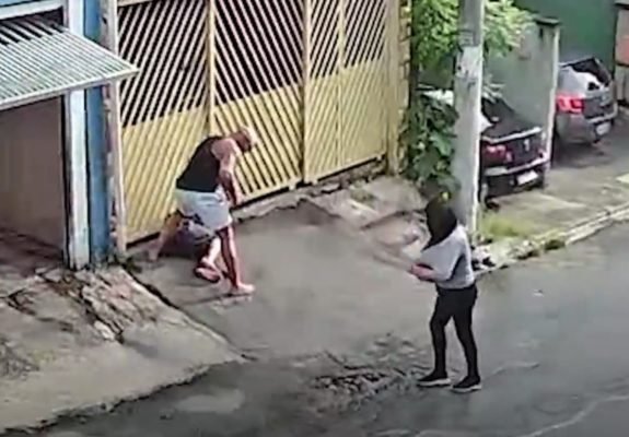 Imagem de homem rendendo outro na calçada; mulher olha para camiseta suja de sangue - Metrópoles