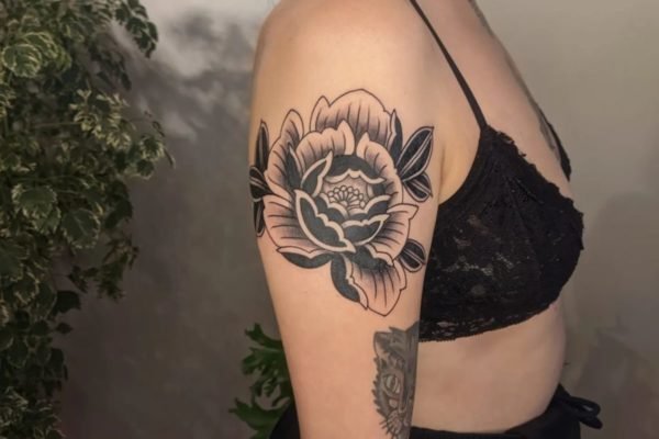 Mulher branca de lado com uma flor tatuada no braço