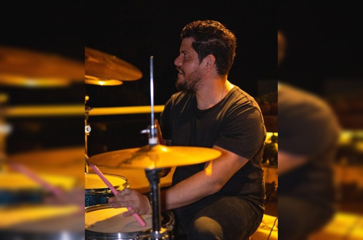Imagem colorida de homem com camisa preta tocando bateria