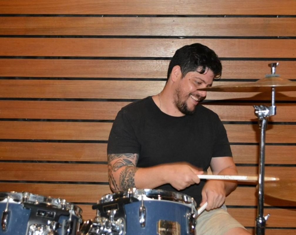 Imagem colorida de homem com camisa preta tocando bateria