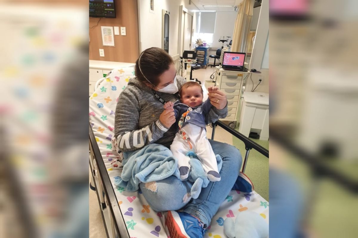 Foto mostra mulher em cama de hospital com bebê em seus braços