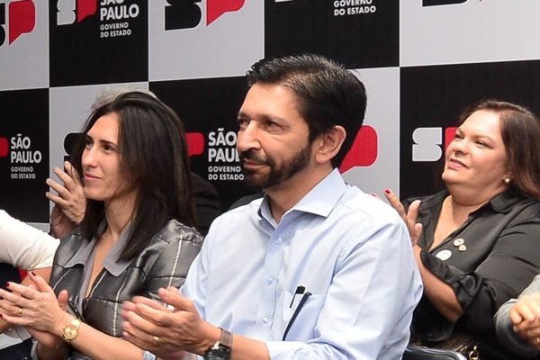 Imagem colorida mostra Ricardo Nunes, de camisa branca, batendo palma sentado e sorrindo - Metrópoles