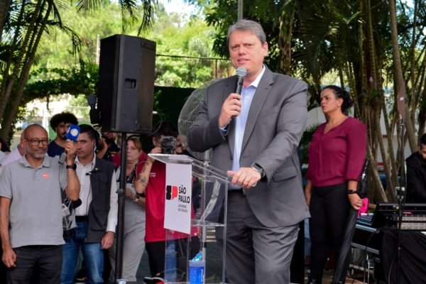 Imagem colorida mostra o governador Tarcísio de Freitas fazendo discurso em São Paulo; ele veste um terno cinza e uma camisa azul clara, sem gravata - Metrópoles