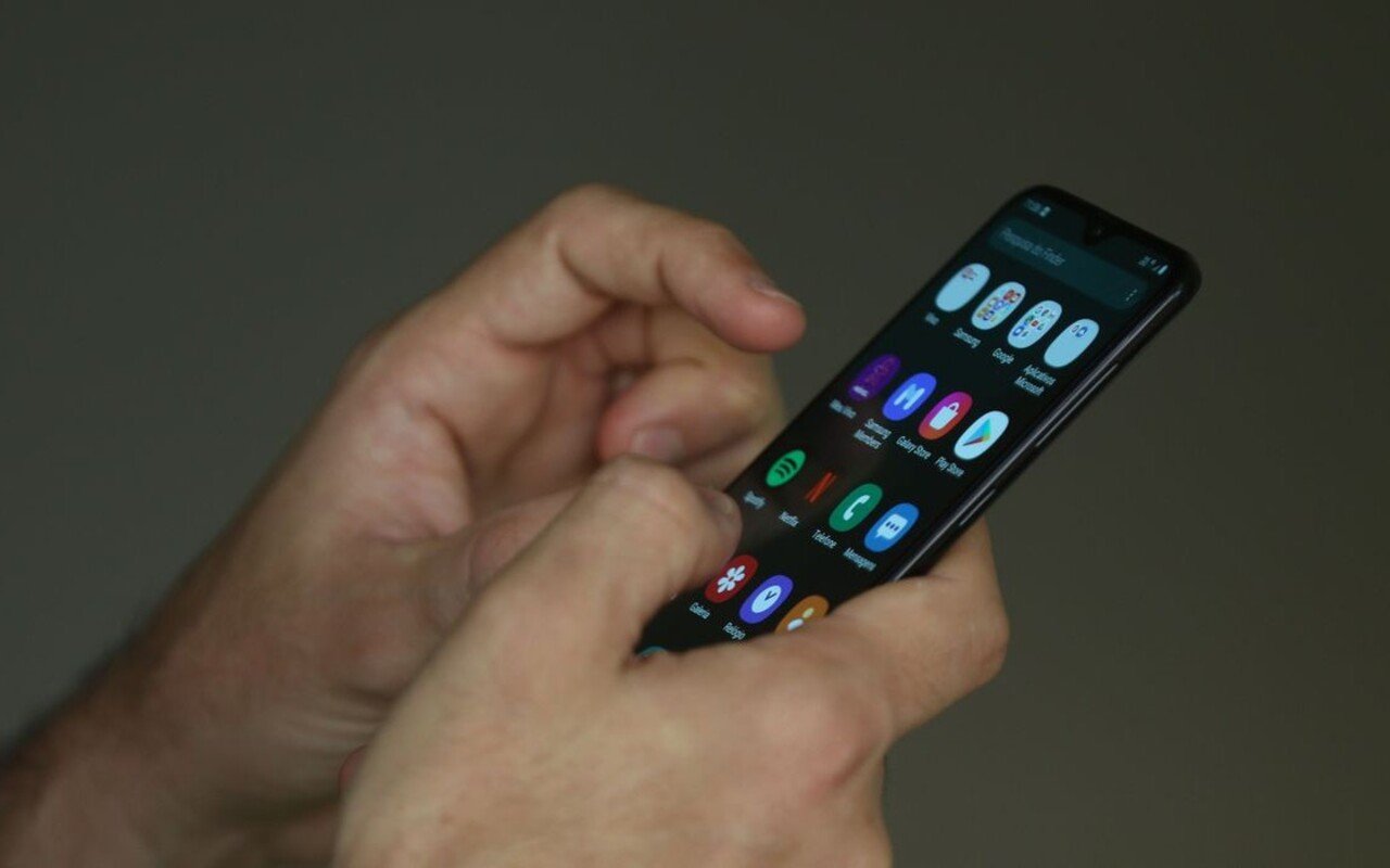 Imagem colorida de mão segurando celular - Metrópoles