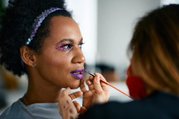 Foto colorida de uma mulher se maquiando - Metrópoles