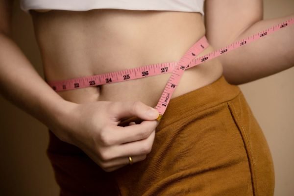 mulher medindo a gordura da barriga com fita métrica