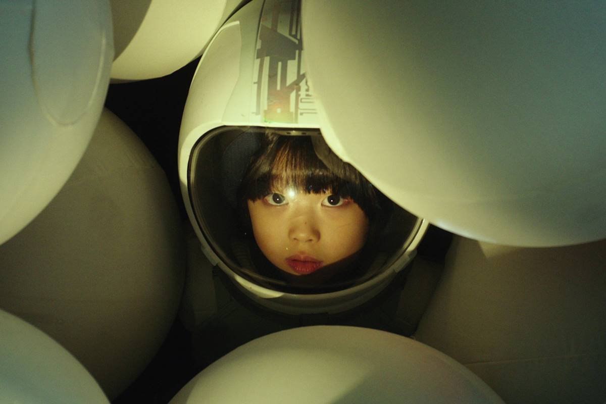 Menina com capacete branco em meio a diversos balões brancos 