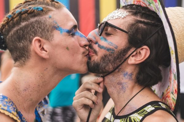 Imagem mostra dois homens com maquiagem de glitter se beijando no Carnaval - Metrópoles