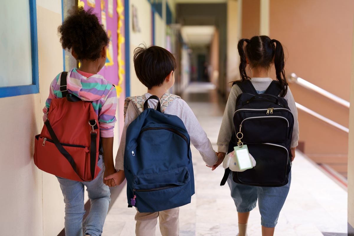 Fotografia mostra três crianças de costas, de mãos dadas. Todas estão de mochila nas costas; governo de SP proibiu o uso de alguns aplicativos nas salas de aula - Metrópoles
