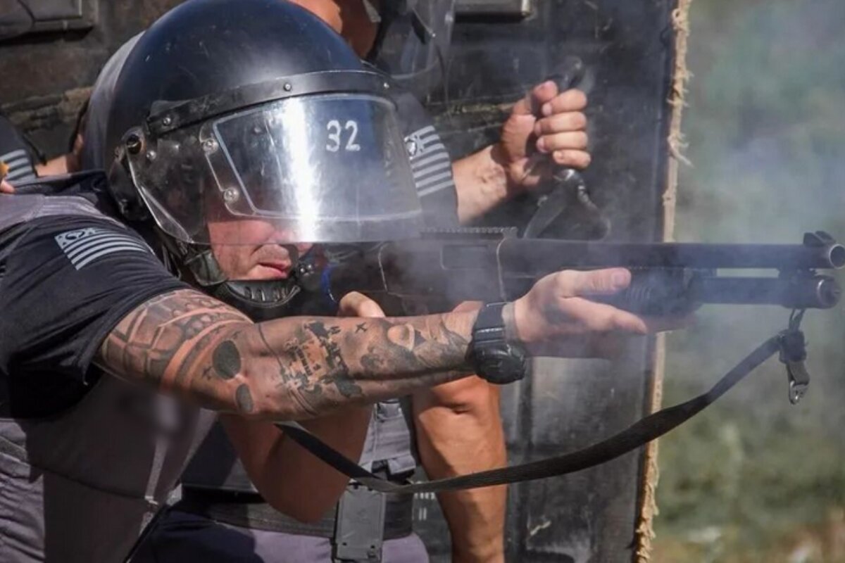 Em foto colorida PM com capacete e fardado atira com escopeta calibre 12 - Metrópoles