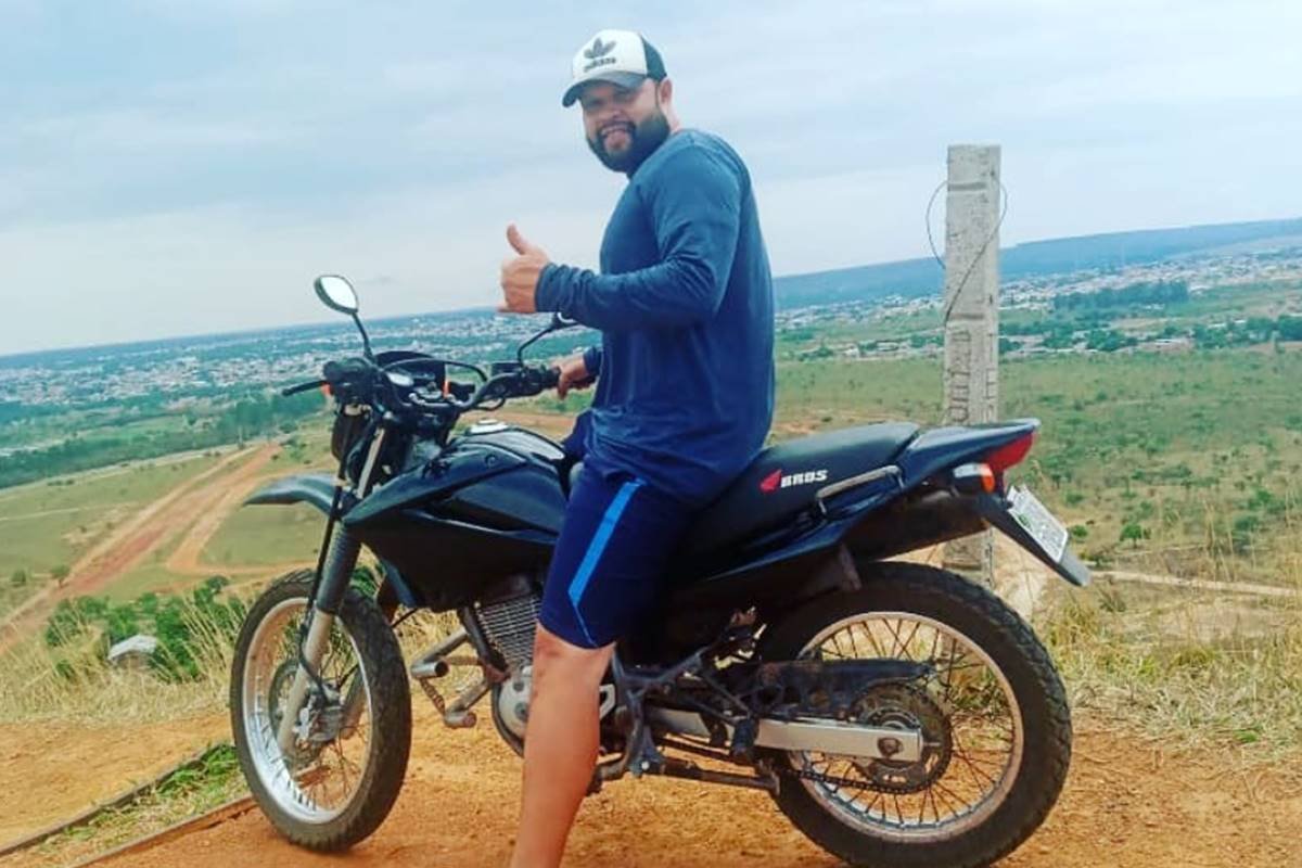 Homem de barba de camisa azul montado em uma moto e usando boné