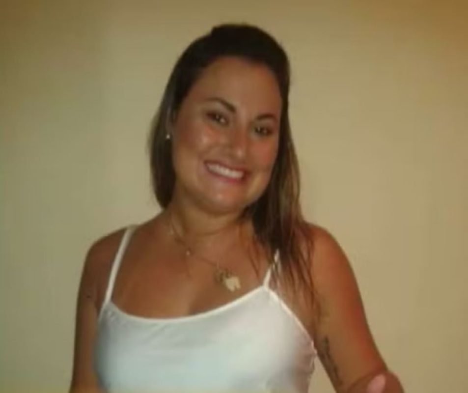 Imagem colorida mostra Dayane Isabel Roncari, uma mulher branca, de cabelos loiros, vestindo uma camiseta regata branca, sorrindo para a câmera - Metrópoles