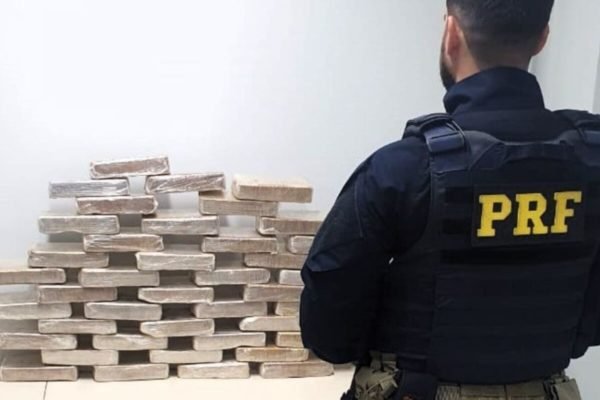 Na imagem, agente da PRF posa ao lado de tabletes de cocaína apreendidos