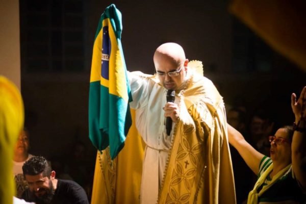 O padre José Eduardo de Oliveira e Silva segura bandeira do Brasil durante missa em outubro de 2018 - Metrópoles