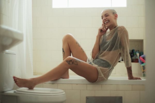 Jovem mulher sentada em box de banheiro sorrindo - Metrópoles