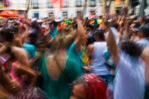 Foto colorida e embaçada de pessoas brincando carnaval em um bloco de rua - metrópoles