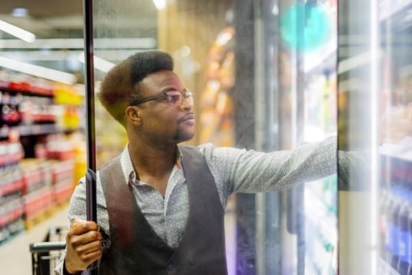 Homem negro escolhendo bebida em freezer de supermercado - Metrópoles