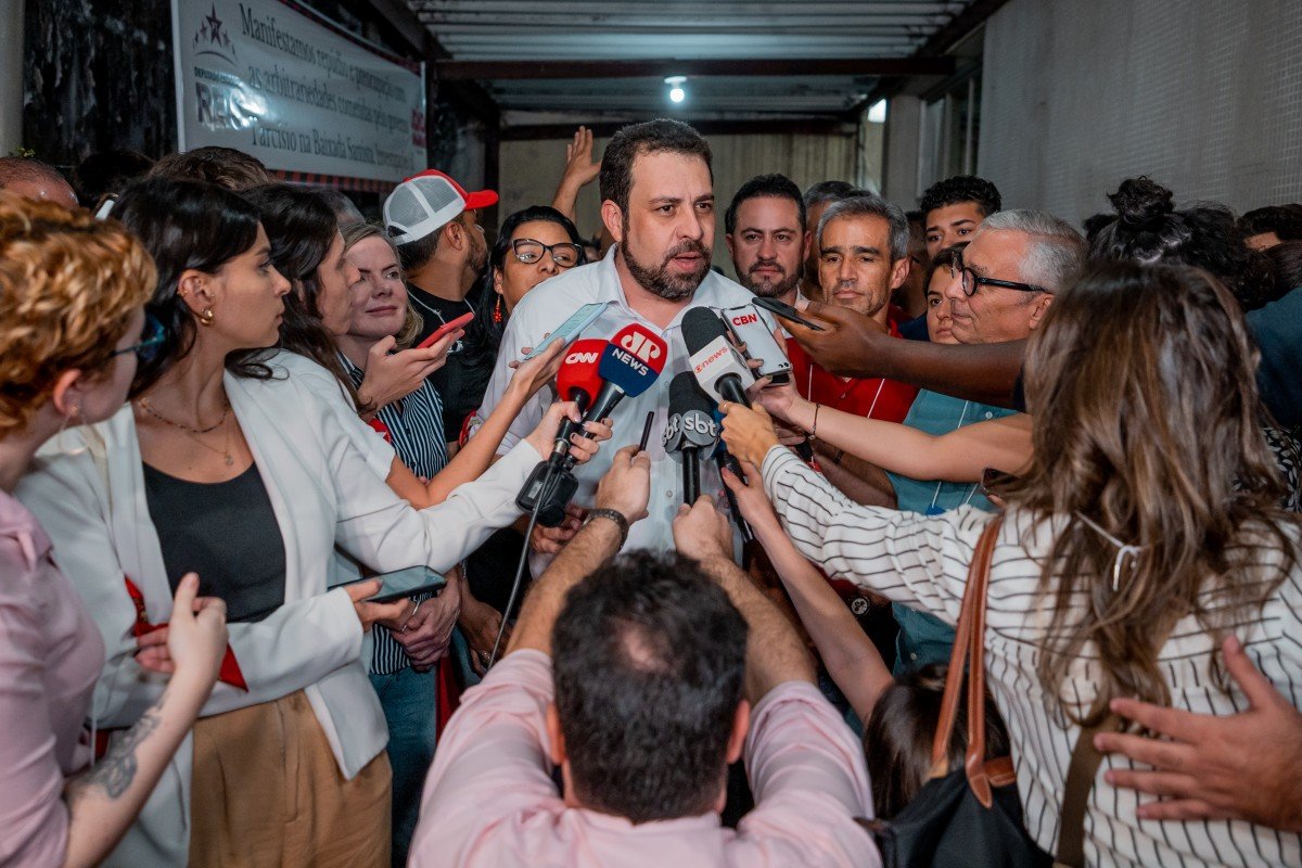 Imagem colorida mostra Boulos no centro de uma roda de jornalistas, que o entrevistam - Metrópoles