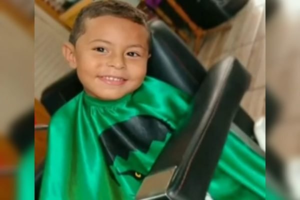 Imagem de menino sorrindo com capa de proteção verde - Metrópoles