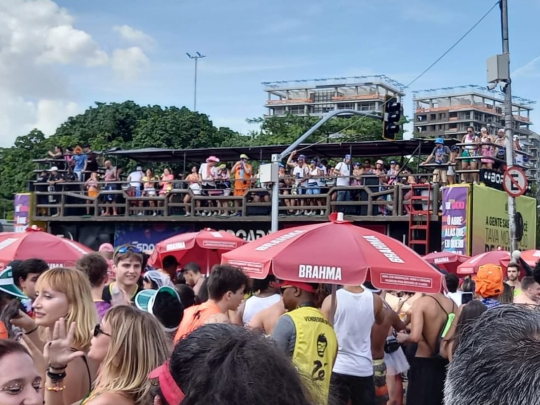 Imagem colorida mostra bloco de Carnaval Vou de Táxi, no fundo, com foliões dançando no Carnaval - Metrópoles