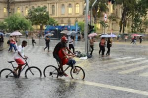 foto colorida de pedestres e ciclistas enfrentando pontos de alagamento no centro de SP durante chuva - Metrópoles