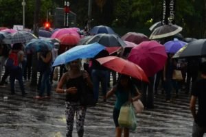 foto colorida de pedestres caminhando com guarda-chuvas em meio à chuva no centro de SP durante chuva - Metrópoles