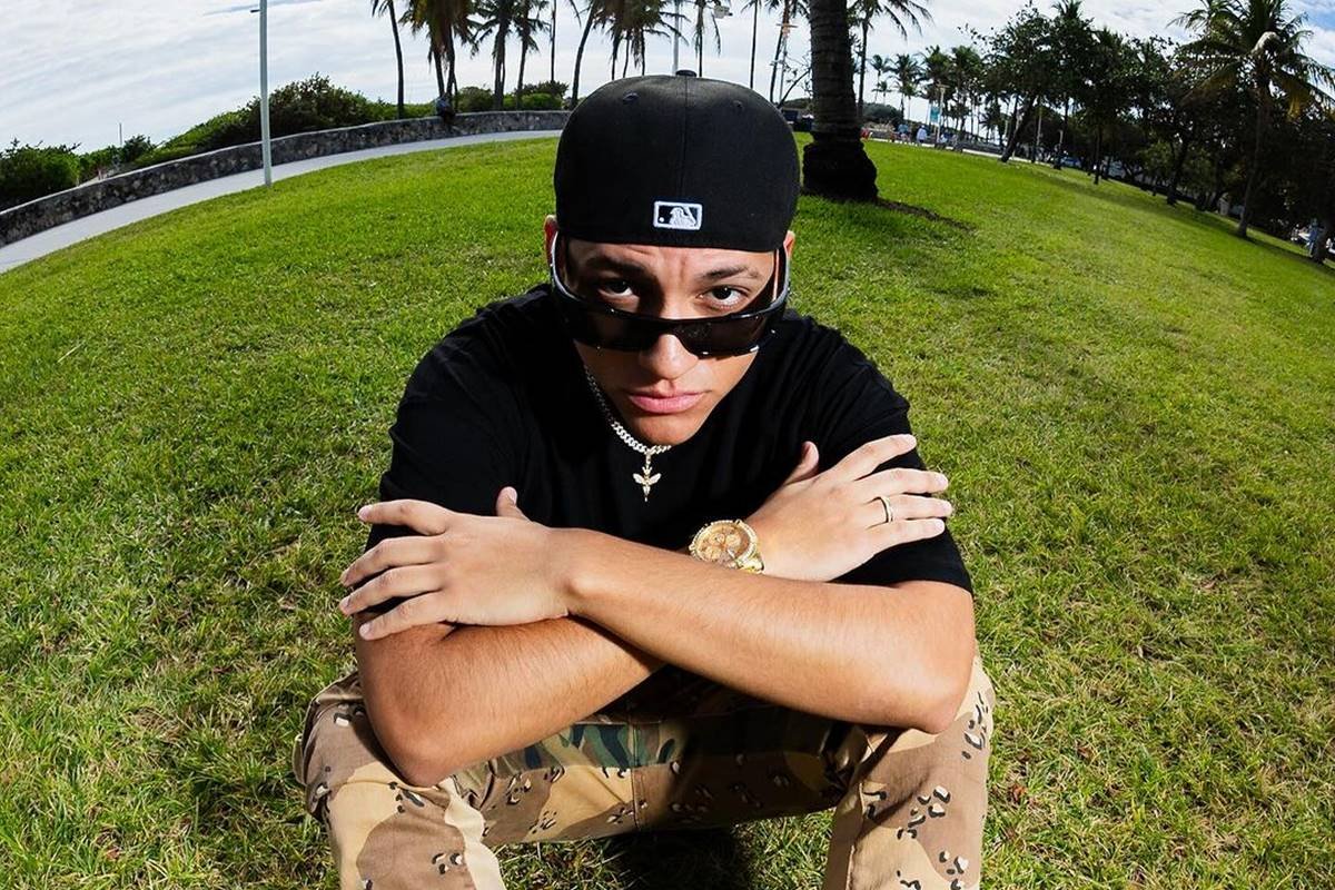 foto colorida de homem latino posando de camiseta preta, bone e oculos escuros - metrópoles