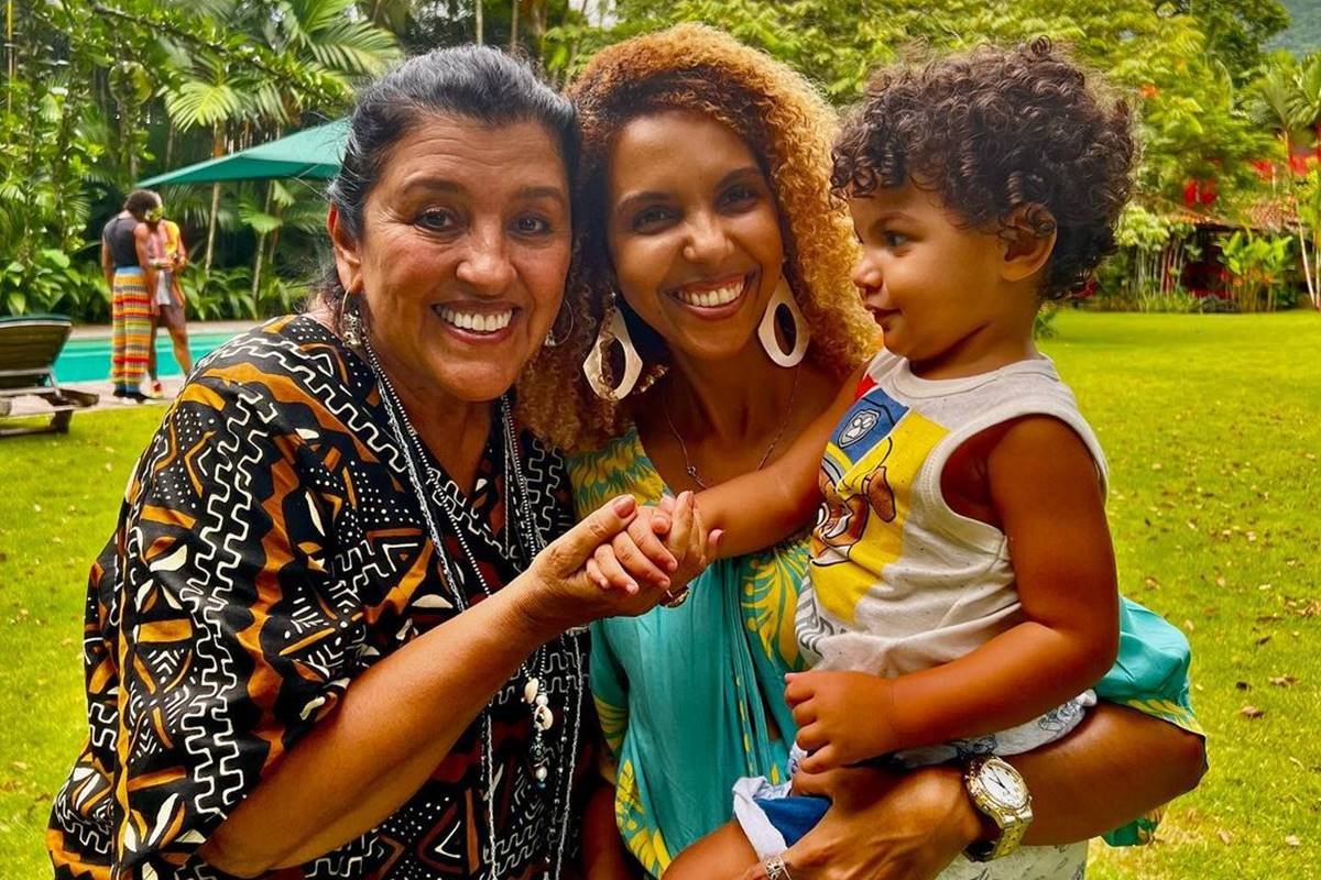 foto colorida de rosto de mulher negra sorrindo com bebe no colo ao lado de regina casé - metrópoles