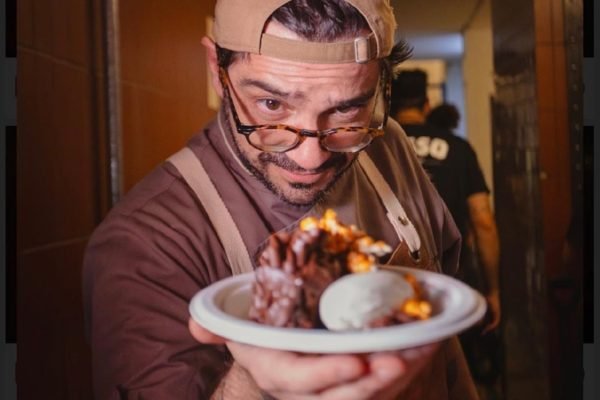 Chef do GNT, Lucas Corazza posa com o boné para trás e um prato na mão - Metrópoles