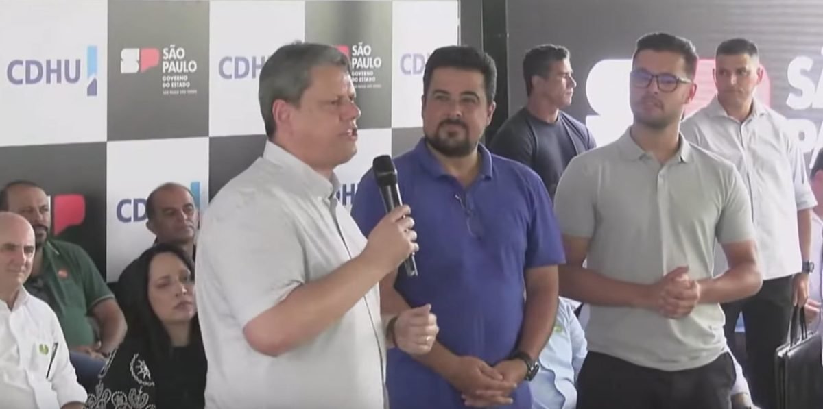 Imagem de Tarcísio de Freitas com microfone na mão ao lado de Felipe Augusto