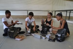 foto colorida de quatro alunos de balé abrindo os kits com uniforme e sapatilhas de dança - Metrópoles