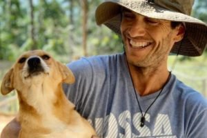 Cachorro caramelo ao lado de homem de chapéu sorrindo - Metrópoles