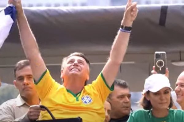 Homem branco vestindo camiseta da Seleção Brasileira ergue as mãos em direção ao céu