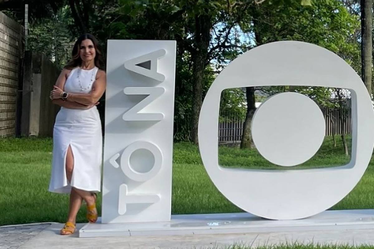 A color photo of Fatima Bernardes leaning on a totem written on NA next to the Globo logo - Capitals