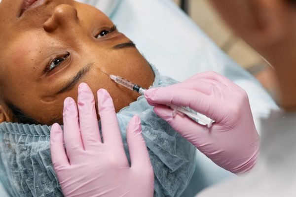 Mãos de médica aplicando injetável em testa de mulher negra - Metrópoles