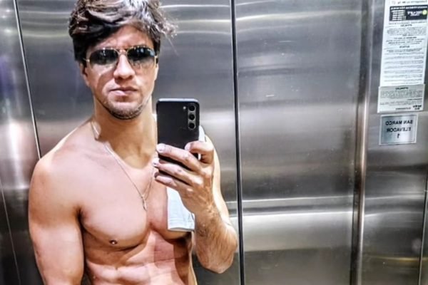 Léo San posa no espelho do elevador, sem camisa e de óculos escuros - Metrópoles