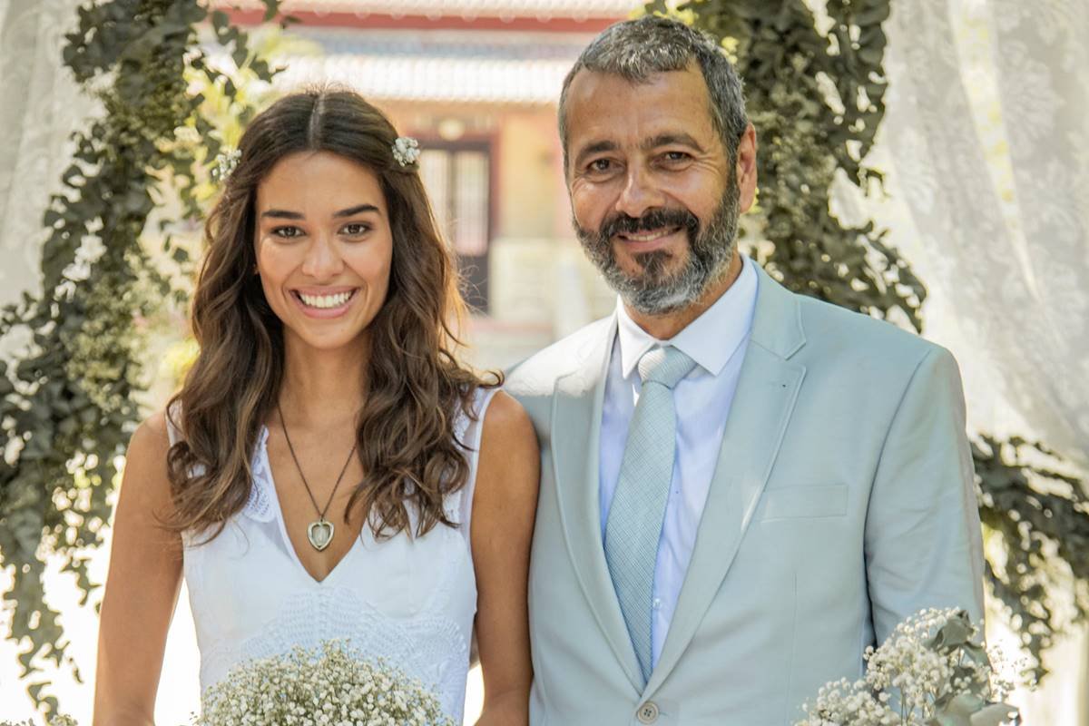 foto colorida de mulher de cabelos castanhos vestida de noiva ao lado de marcos palmeira de terno cinza - metrópoles