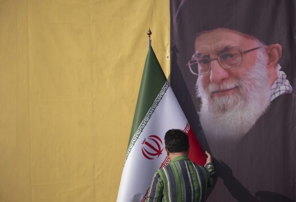 Imagem colorida mostra homem segurando a bandeira do Irã e a foto do aiatolá Ali Khamenei ao fundo - Metrópoles