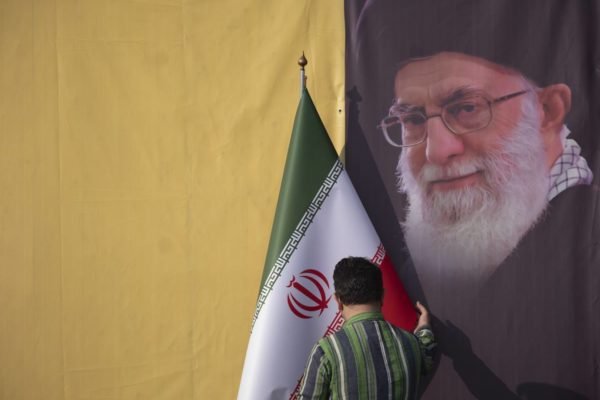 Imagem colorida mostra homem segurando a bandeira do Irã e a foto do aiatolá Ali Khamenei ao fundo - Metrópoles