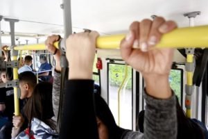 Imagem colorida de mãos segurando barra de ônibus