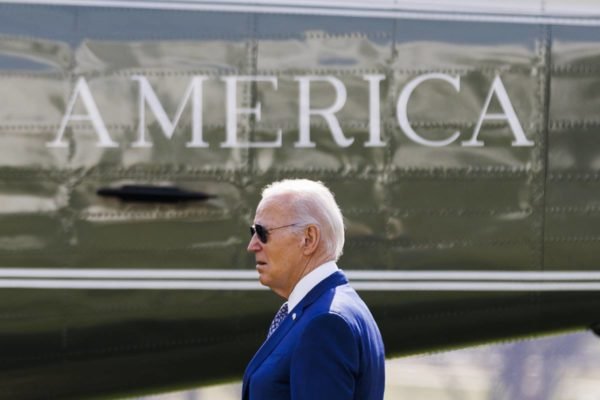 Imagem colorida mostra Joe Biden perfilado atrás de uma logo escrito "America" - Metrópoles