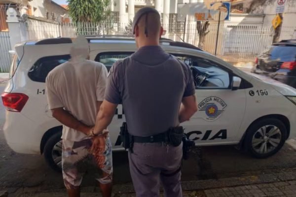 Imagem colorida mostra homem algemado ao lado de policial militar; ele foi preso por agredir a mulher após ela se recusar a ter relações sexuais com ele - Metrópoles