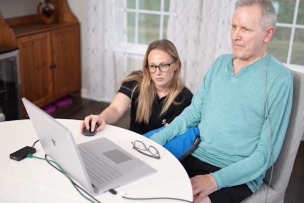 Homem sentado olhando para computador a lado de mulher abaixada - Metrópoles