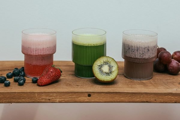 Três copos um ao lado do outro. Um com suco de morango, outro de kiwi e outro de uva