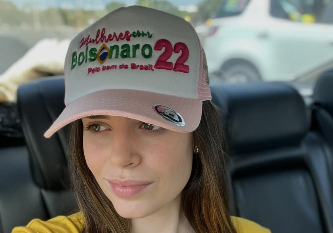 Zoe Martinez, mulher branca de cabelos lisos e boné, sentada em banco traseiro de um carro e olhando para o lado - Metrópoles