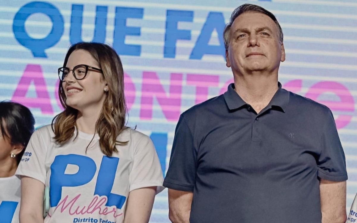 Zoe Martinez e Jair Bolsonaro; ela usa óculos e olha para o lado, enquanto ele olha para frente; os dois estão em um palco - Metrópoles