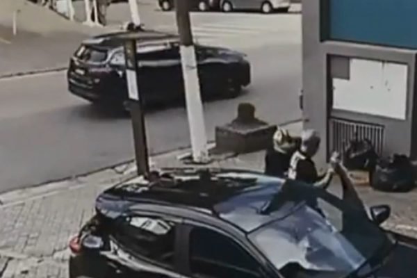 Imagem colorida mostra bandido abordando o pai do cantor MC Gui para roubar o carro em um estacionamento no Tatuapé, zona leste de São Paulo